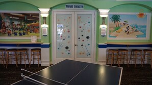 Una habitación con mesa de ping pong, cartel de cine y un mural con escena de playa.