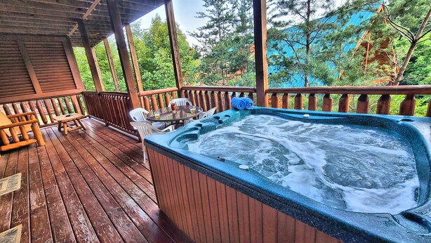 A wooden deck with a hot tub, outdoor seating, and a view of trees.
