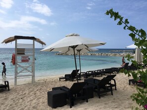 A beach with lounge chairs, umbrellas, and a lifeguard tower.