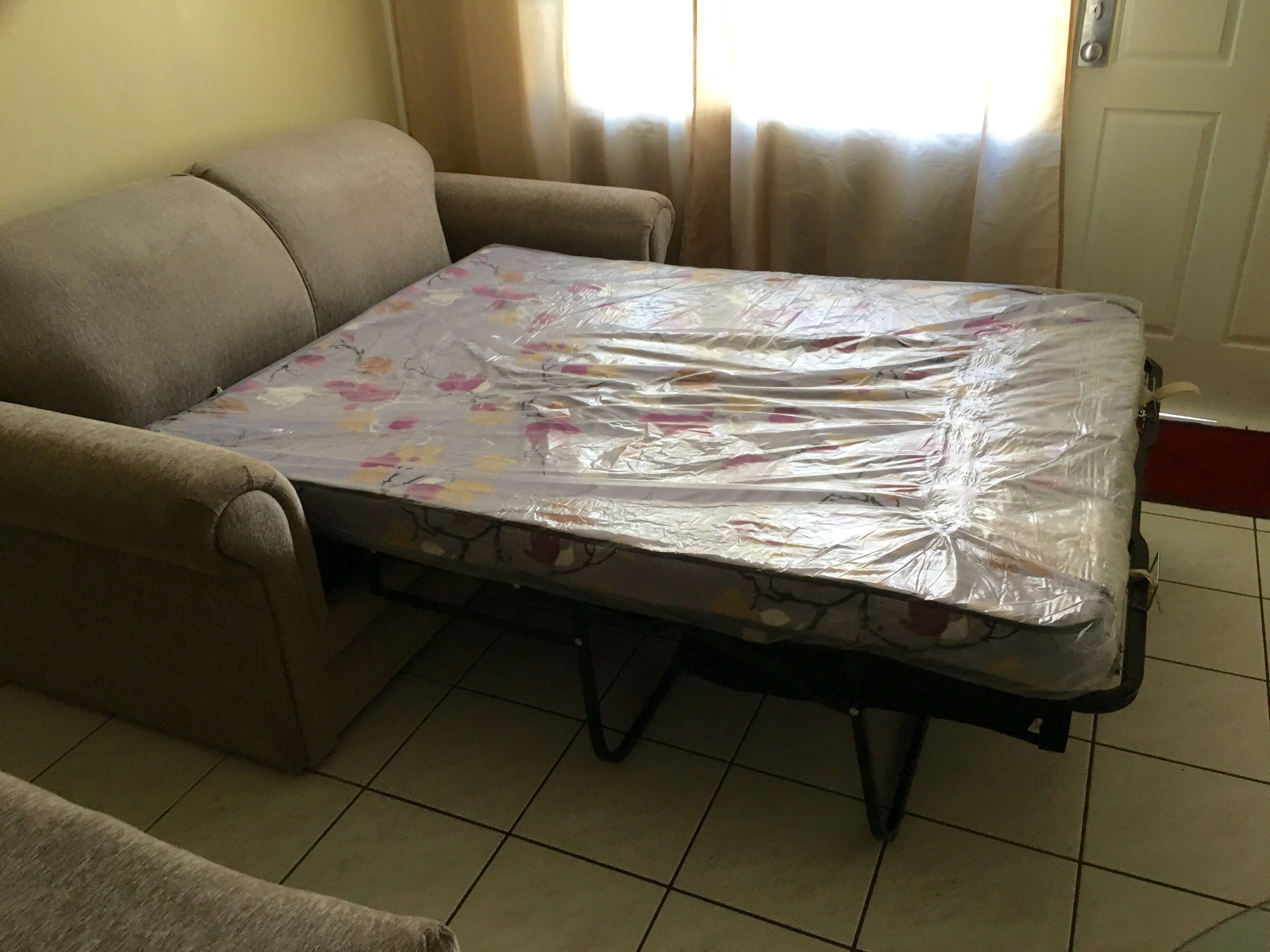 A living room with a sofa and a mattress on the floor.