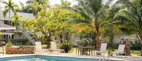 Un área de piscina con sillones de descanso y palmeras.