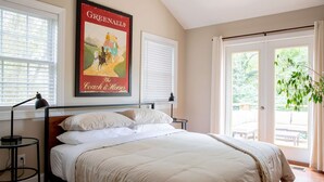 A bedroom with a bed, two bedside tables, a poster, and a view of the outdoors.