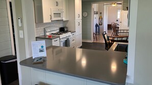 Une cuisine moderne avec des meubles blancs, une cuisinière à gaz, un four à micro-ondes et un grille-pain. On y trouve également un coin repas avec une table et des chaises.