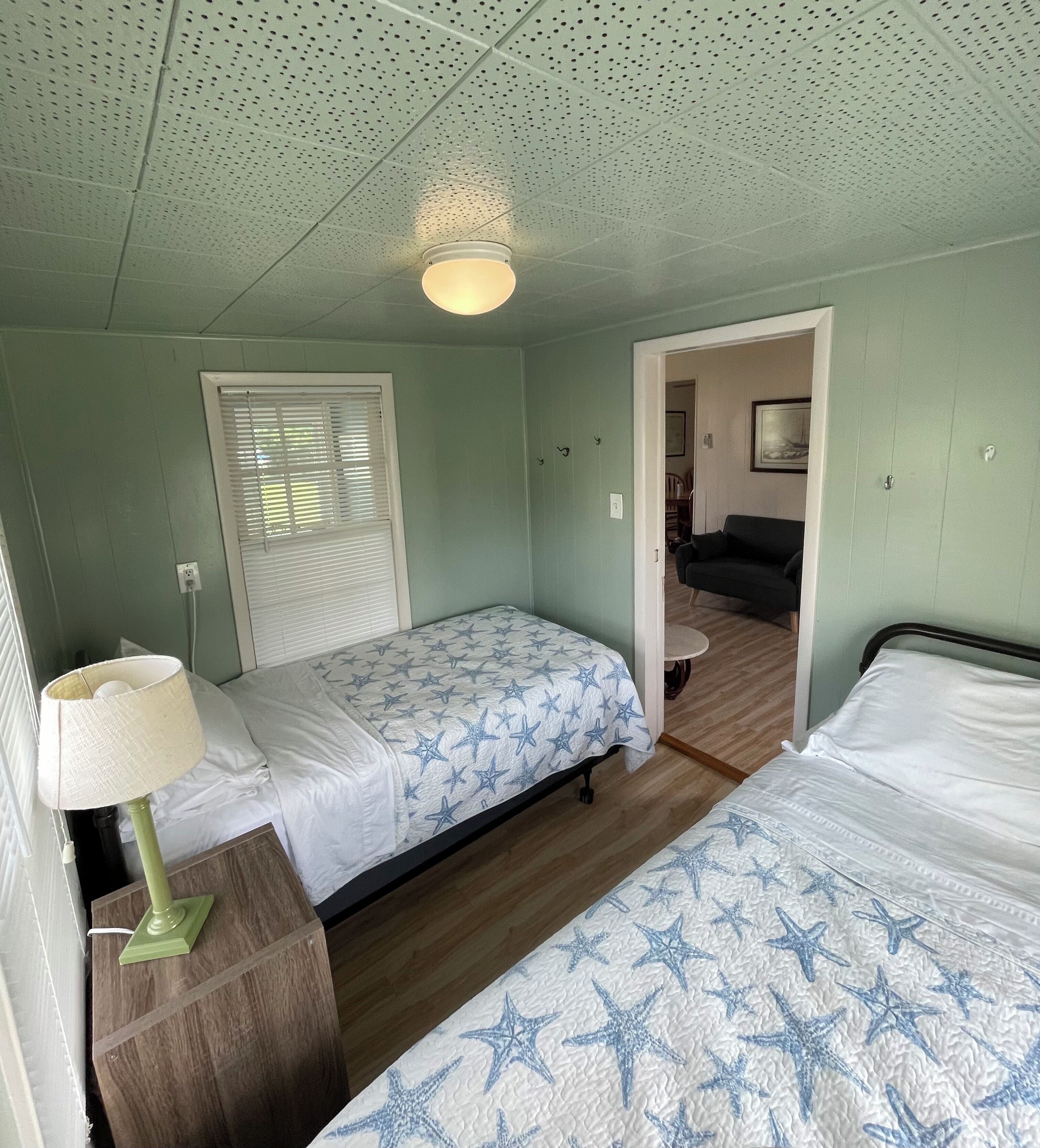 Een kamer met twee bedden, een lamp, een plafondlamp en een deur naar een andere kamer.