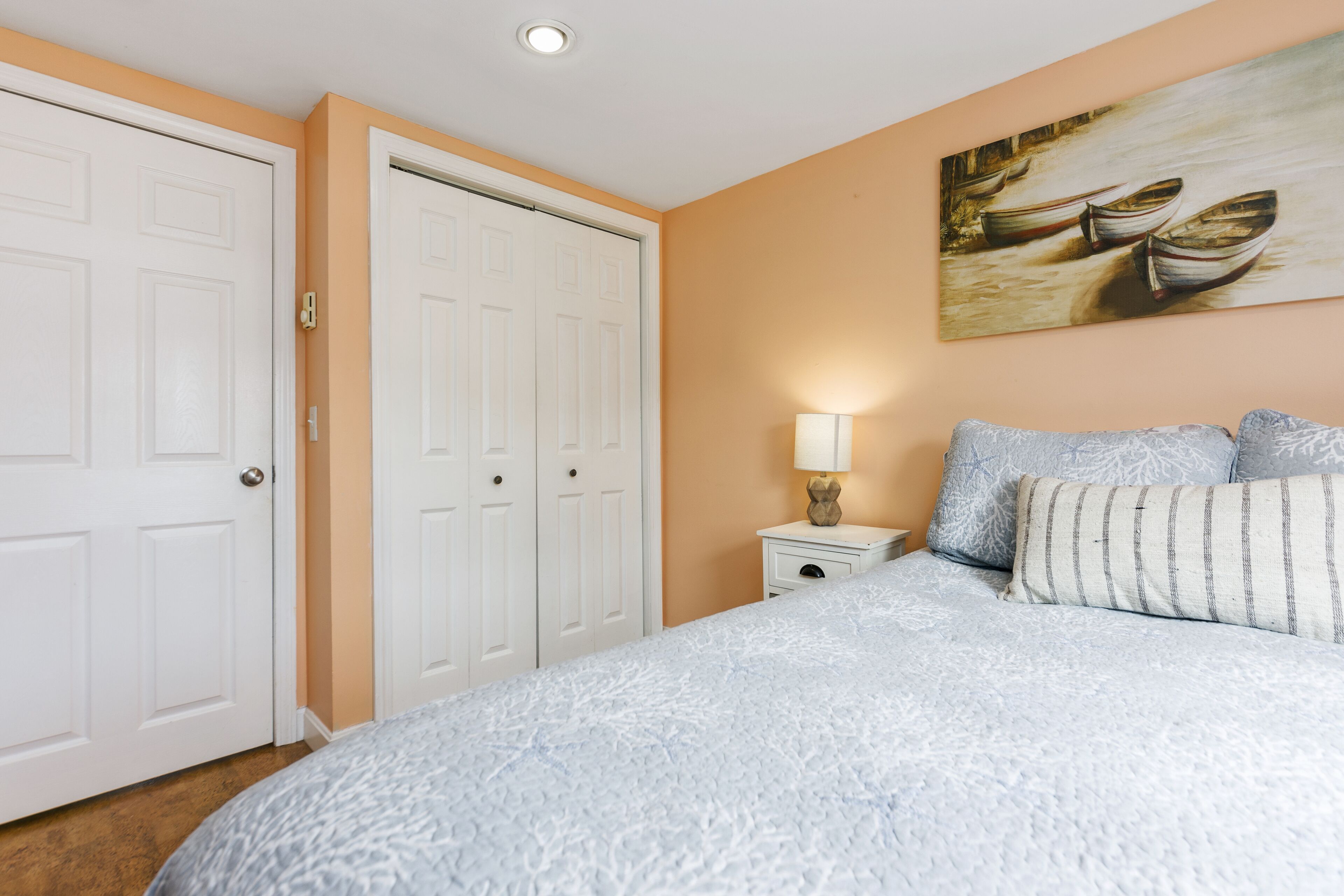 Une chambre à coucher avec un grand lit, une armoire blanche et un tableau représentant des bateaux accroché au mur.