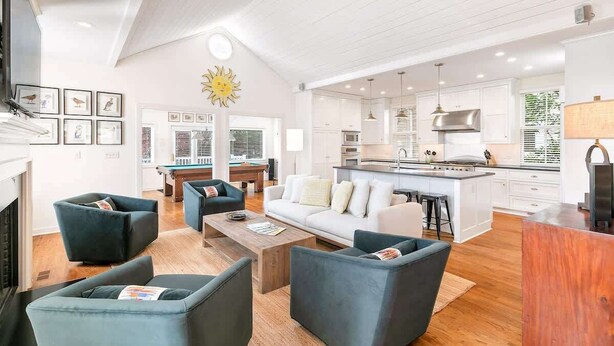 Una sala de estar moderna con chimenea, mesa de billar y cocina con armarios blancos y una isla grande.