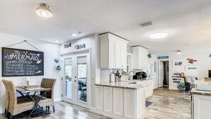 A kitchen with white cabinetry, a dining area with wicker chairs, and a chalkboard menu.