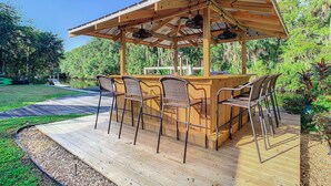 A wooden deck with a bar area, outdoor chairs, and a pergola with fans.