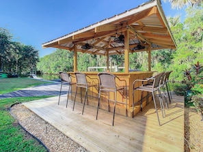 Terraza de madera con zona de bar, sillas exteriores y una pérgola con ventiladores.