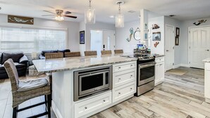 A modern kitchen with a marble countertop, stainless steel appliances, and a ceiling fan.