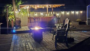 An outdoor patio area with a wooden deck, a covered seating area, and a fire pit.