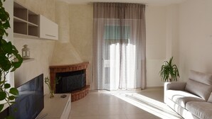 A living room with a fireplace, a flat-screen TV, a sofa, and a large window with sheer curtains. - Appartamento in zona Panoramica a due passi dal Mare ed immerso nel verde (Gabicce Monte)