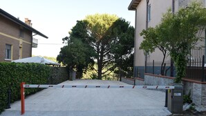 A gated entrance with a metal barrier, a tree, and a building with a balcony. - Appartamento in zona Panoramica a due passi dal Mare ed immerso nel verde (Gabicce Monte)
