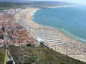 A coastal town with a beach lined with rows of beach umbrellas and sun loungers.
