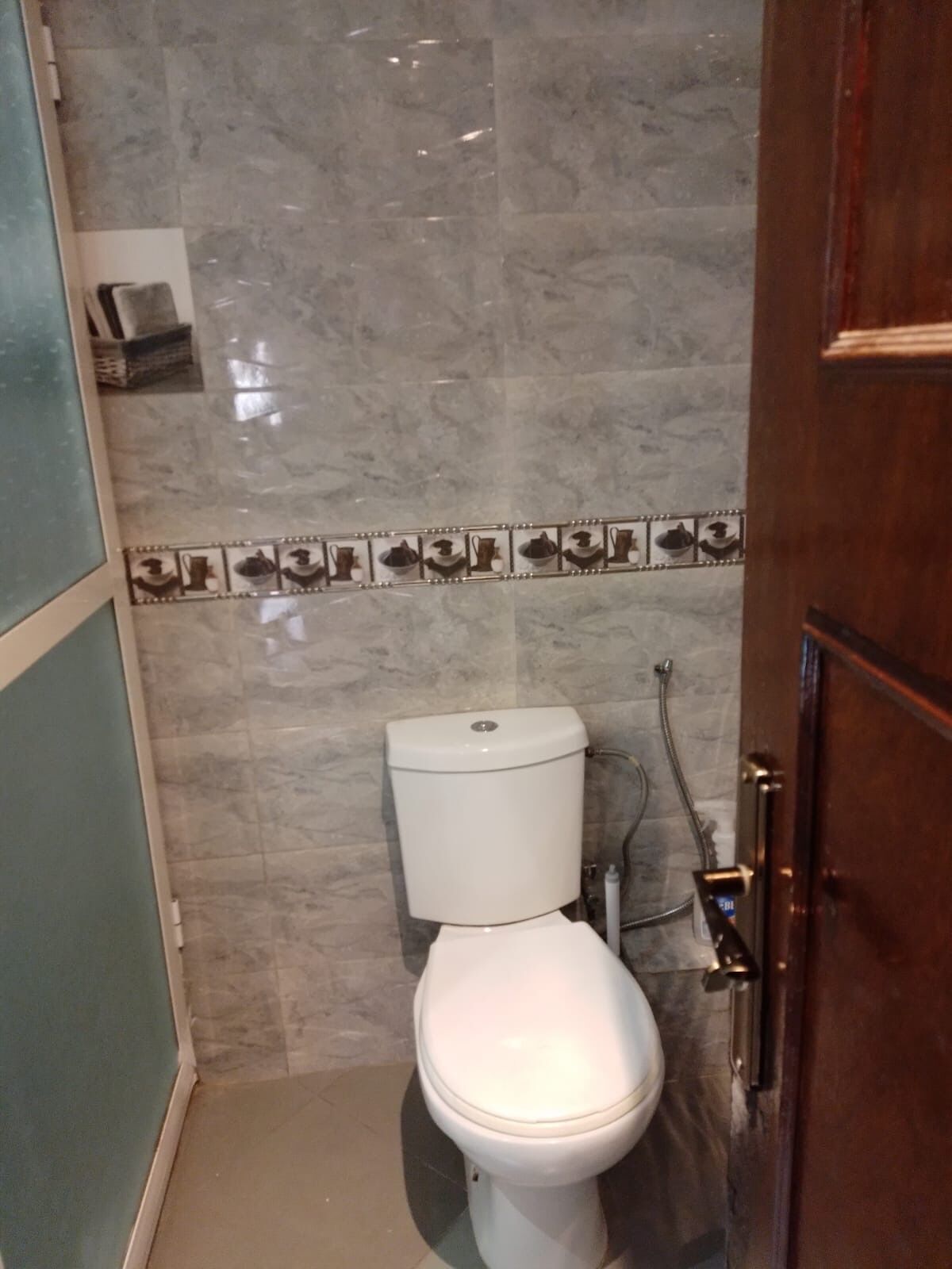 A bathroom with a toilet, a shower, and a tiled wall.