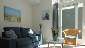 Un salon moderne avec un canapé bleu foncé, un fauteuil en osier, une petite table ronde et deux tableaux accrochés aux murs.