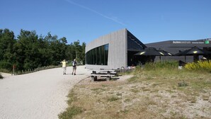 Un bâtiment moderne à la façade incurvée et aux grandes fenêtres, situé à côté d’un sentier et bordé d’arbres.