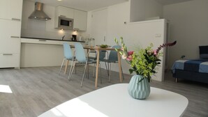 Une cuisine moderne avec des armoires blanches, un four à micro-ondes et une cuisinière. On y trouve un coin repas avec une table blanche et des chaises bleues. Un vase rempli de fleurs est posé sur la table.