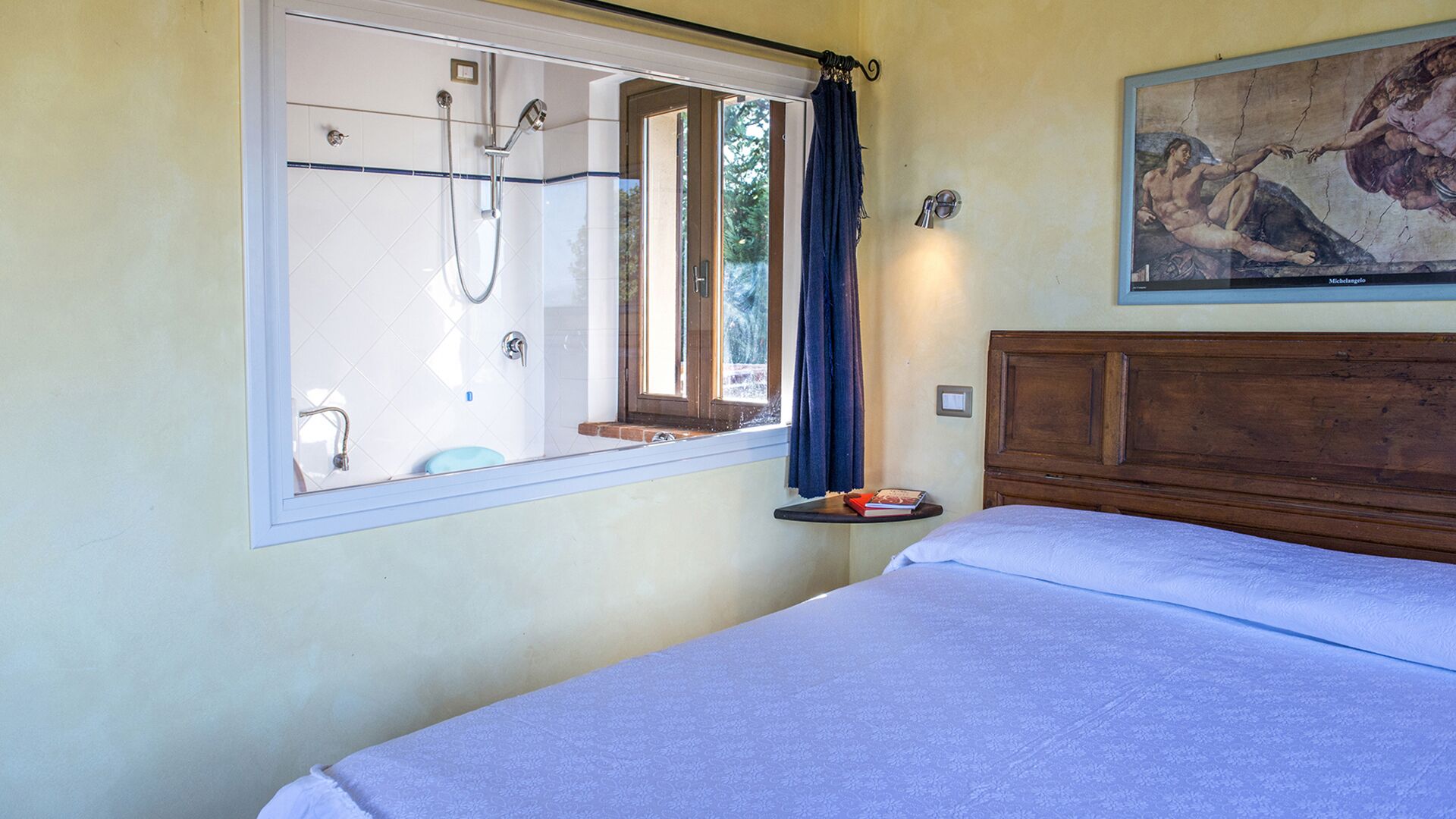 A bedroom with a bed, a window with a shower, and a painting on the wall.