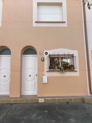 A building facade with two white doors, a window with a metal grill, and a sign indicating a parking restriction. - Townhouse for rent in the summer season Estartit (L'ESTARIT)