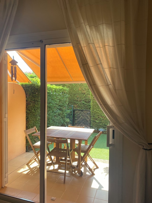 An outdoor patio with a table and chairs, a yellow awning, and a green hedge in the background. - Townhouse for rent in the summer season Estartit (L'ESTARIT)