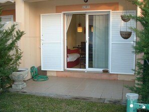 A hotel entrance with a sliding glass door, a small outdoor seating area, and a potted plant on the left.