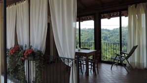 A covered outdoor area with a table and chairs, a view of a forested landscape, and a balcony with a railing. - Isolated on hill, flat with terrace,garden among romanesque art,quiet,nature (cocconato)