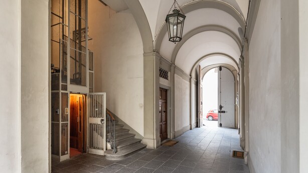 A hallway with stone flooring, a staircase, and arched ceilings.
