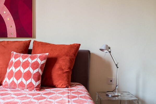A neatly made bed with patterned bedding, a modern lamp on a side table, and a piece of abstract art on the wall.