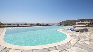 Una piscina con deck de piedra, sillas de descanso y vista al mar.