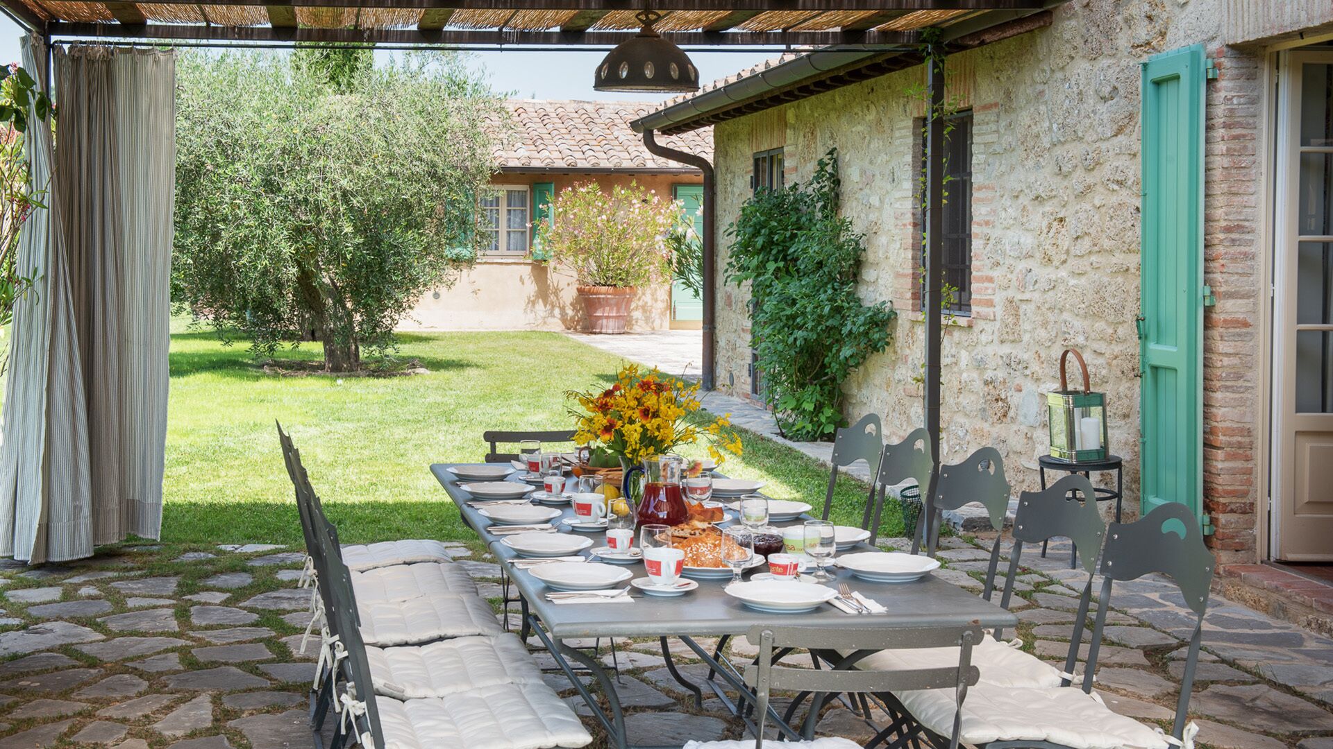 Un espace de restauration en plein air avec une table en pierre dressée pour un repas, entourée d’escaliers en pierre et de verdure.