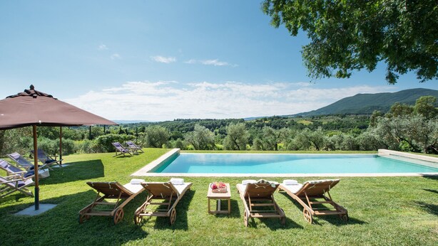 Un área de piscina con sillones de descanso y una pérgola, rodeada de exuberante vegetación y montañas al fondo.