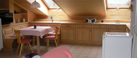 Una cocina compacta con armarios de madera, una mesa de comedor con sillas, un refrigerador pequeño y un televisor.