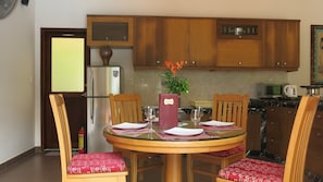 A dining area with a round table, four wooden chairs, a menu stand, a refrigerator, a microwave, and a small potted plant.