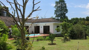 A house with a swimming pool, surrounded by lush greenery and a clear sky.