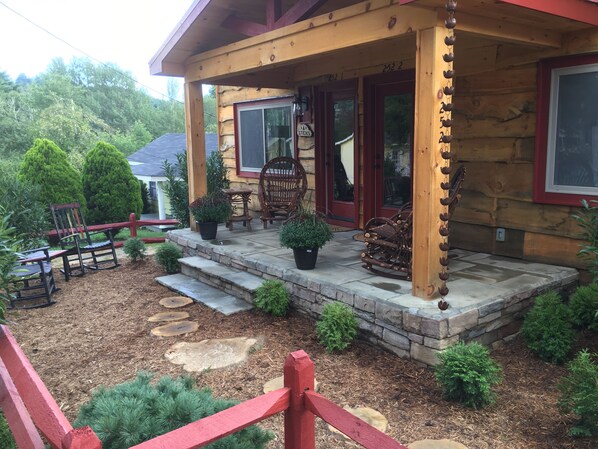 Une cabane en bois avec un porche, des marches en pierre et un espace salon extérieur.