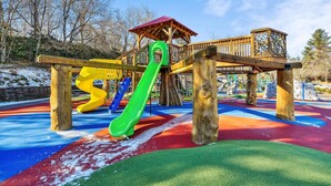 A playground with a green slide, a yellow spiral slide, and a wooden climbing structure. - Downtown Main Street "STONES" FENCED YARD (Blowing Rock)