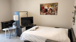 Una moderna camera d'hotel con un letto, una scrivania con televisore, una sedia e un quadro appeso al muro.