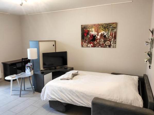 Une chambre d’hôtel moderne, équipée d’un lit, d’un bureau avec une télévision, d’une chaise et d’un tableau au mur.