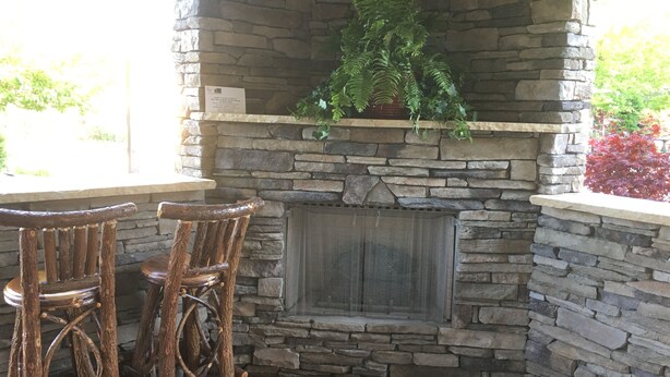 A stone fireplace with a green plant on top, two wooden chairs, and a stone wall.