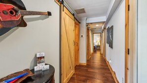 A hallway with wooden floors, a guitar on the wall, and a desk with business cards and a brochure.