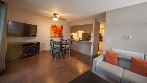 A modern living room with a sofa, a dining area with chairs and a table, a kitchen with a refrigerator and stove, and a TV mounted on the wall. - Stylish/Clean 1BD/BA Pointe Royale - Close to Pool - Great Guest Reviews (Branson)