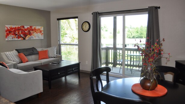 A living room with a sofa, coffee table, and chairs, a dining table with a vase of flowers, and a large window with a view of greenery. - Stylish/Clean 1BD/BA Pointe Royale - Close to Pool - Great Guest Reviews (Branson)