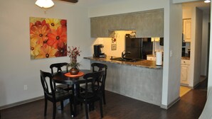 A dining area with a table and chairs, a ceiling fan, a kitchen with a refrigerator, and a painting on the wall. - Stylish/Clean 1BD/BA Pointe Royale - Close to Pool - Great Guest Reviews (Branson)