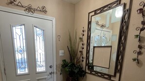 Un couloir avec une porte blanche, un grand miroir et une plante en pot.