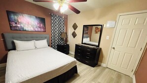Une chambre à coucher avec un lit, une commode, un miroir et un ventilateur de plafond.