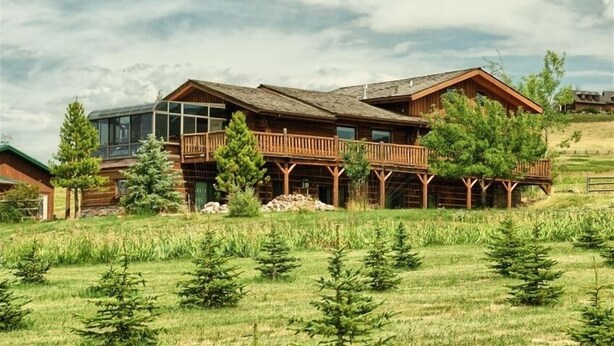A large wooden cabin with a balcony, surrounded by a grassy field and trees. - Comfy Country Condo (West) on 10 Acres between Bozeman & Big Sky (Gallatin Gateway)