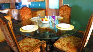 Un coin repas avec une table en verre entourée de chaises à motifs floraux, un saladier rempli de fruits et des verres à vin.