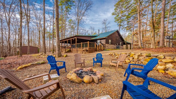 Eine rustikale Holzhütte mit Veranda und Feuerstelle, umgeben von Adirondack-Stühlen.