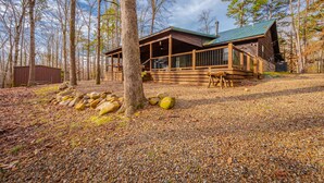 Eine Holzhütte mit einer Holzterrasse, umgeben von Bäumen und Kieselsteinen.